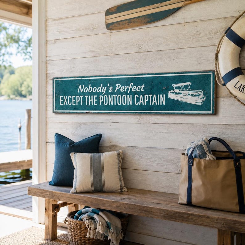 Op de afbeelding: Een rechthoekig blauwgroen bord met witte tekst Nobody's Perfect EXCEPT THE PONTOON CAPTAIN, voorzien van een witte lijntekening van een pontonboot aan de rechterkant. Het bord is bevestigd aan een wand van lichte, horizontale houten planken.