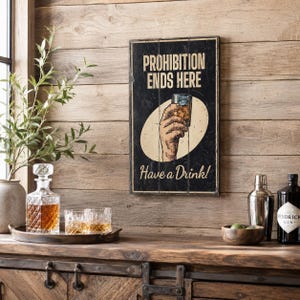 May include: A rectangular wooden wall sign with a black background and distressed finish. It features the text PROHIBITION ENDS HERE and Have a Drink! in cream lettering, with a central illustration of a hand holding a glass of amber liquid.