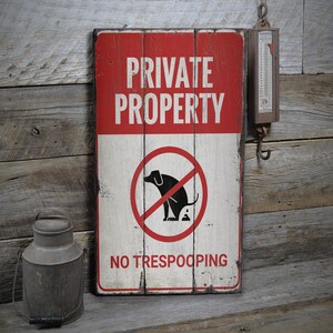 Può includere: Un cartello in legno rustico dipinto di rosso e bianco. Il cartello recita "Proprietà privata" e "Vietato defecare". Una silhouette in bianco e nero di un cane è mostrata in un cerchio rosso con una linea diagonale che lo attraversa.