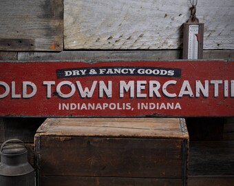 Op de afbeelding: Een rood houten bord met witte tekst die "Dry & Fancy Goods Old Town Mercantile Indianapolis, Indiana" zegt.