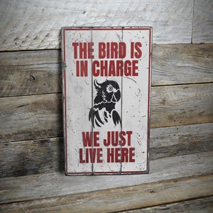 a sign on a wooden wall that says the bird is in charge we just live