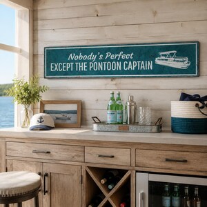 Op de afbeelding: Een rechthoekig blauwgroen wandbord met een witte rand en witte tekst die Nobody's Perfect EXCEPT THE PONTOON CAPTAIN luidt, voorzien van een witte lijntekening van een pontonboot aan de rechterkant tegen een verweerde achtergrond.