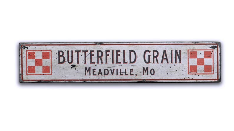May include: A white wooden sign with red and black lettering that reads "Butterfield Grain Meadville, MO". The sign has two red and white checkered squares on either side of the text.