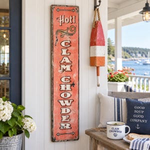 May include: A tall, rectangular, weathered coral-coloured wooden sign with the text "Hot! CLAM CHOWDER" in black and white lettering. The sign features decorative scrollwork and horizontal lines at the top and bottom, with a distressed finish.