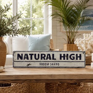 May include: A rectangular white sign with a distressed finish and black border. The text "NATURAL HIGH" is printed in large, bold, black capital letters, with "VRBO# 34490" printed in smaller black text centered underneath the main line.