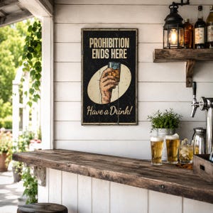 May include: A rectangular wall sign with a black background featuring the text PROHIBITION ENDS HERE at the top and Have a Drink! at the bottom. The center displays an illustration of a hand holding a glass of amber liquid inside an oval.