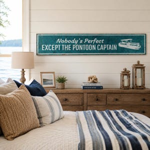 Op de afbeelding: Een lang, rechthoekig houten bord in een blauwgroene kleur met een verweerde afwerking. Het bord bevat witte tekst met de tekst "Nobody's Perfect EXCEPT THE PONTOON CAPTAIN" en een witte lijntekening van een pontonboot aan de rechterkant.