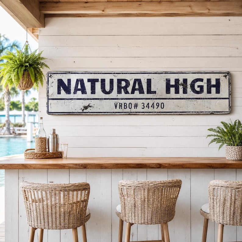 May include: A rectangular metal sign with a distressed white finish and dark blue lettering that reads NATURAL HIGH and VRBO# 34490. The sign features a horizontal line separating the text and has a weathered, vintage-inspired appearance.