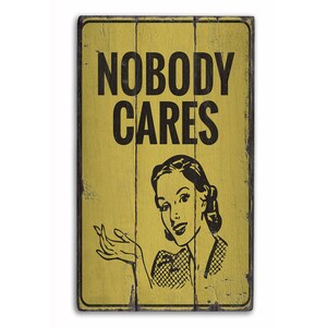 May include: A yellow wooden sign with black text that reads "Nobody Cares". A vintage-style illustration of a woman with a surprised expression is below the text.