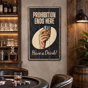 May include: A rectangular black wall sign with a distressed finish featuring the text PROHIBITION ENDS HERE at the top and Have a Drink! at the bottom. In the center, an illustration shows a hand holding a glass of amber-colored liquid.