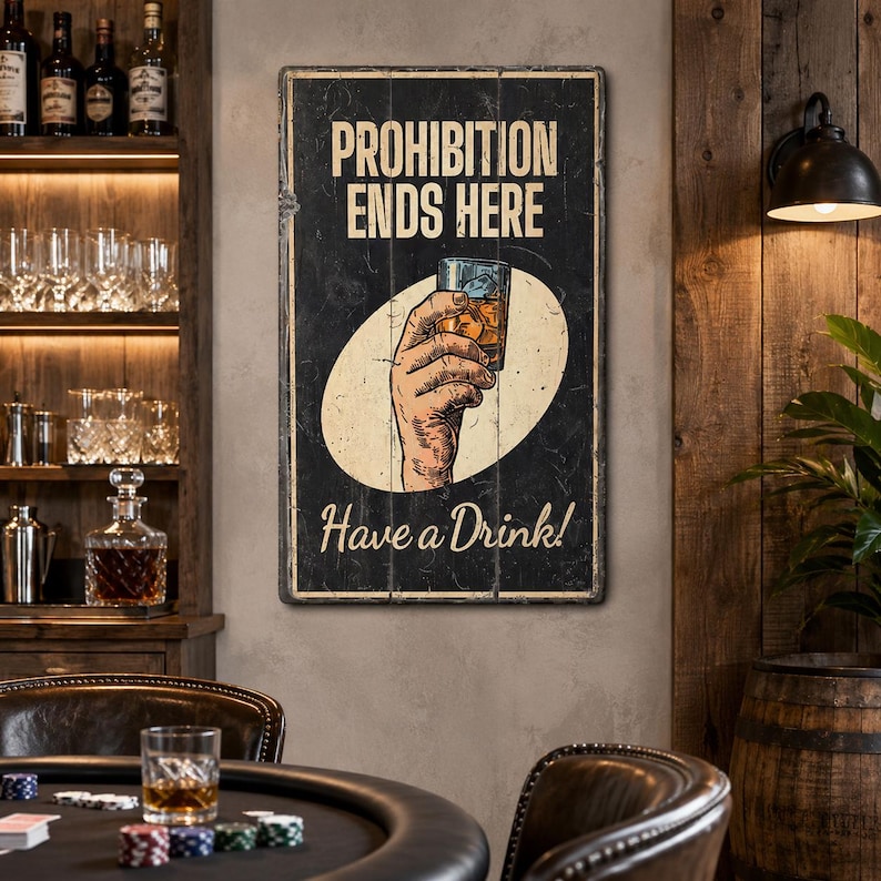 May include: A rectangular black wall sign with a distressed finish featuring the text PROHIBITION ENDS HERE at the top and Have a Drink! at the bottom. In the center, an illustration shows a hand holding a glass of amber-colored liquid.
