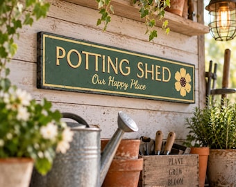 Puede incluir: Un letrero rectangular verde con borde y letras doradas que dice POTTING SHED y Our Happy Place, con un gráfico de flor dorada. El letrero está montado en una pared de madera blanca sobre una regadera galvanizada y una caja de madera.