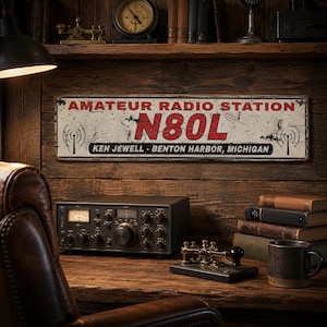 May include: A rectangular metal sign with a distressed white finish, featuring the red text AMATEUR RADIO STATION, the call sign N80L in large red letters, and the black text KEN JEWELL - BENTON HARBOR, MICHIGAN, flanked by two black radio tower icons.