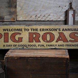 May include: A yellow wooden sign with black lettering that reads "WELCOME TO THE ERIKSON'S ANNUAL PIG ROAST A DAY OF GOOD FOOD, FUN, FAMILY AND FRIENDS".