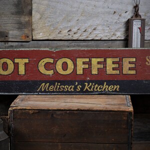 May include: A red and black wooden sign with the text "HOT COFFEE SERVED HERE" in yellow letters. The sign also has the text "Melissa's Kitchen" in white letters.
