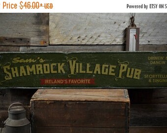 Può includere: Un cartello in legno verde con il testo "Sam's Shamrock Village Pub" in lettere gialle. Il cartello include anche il testo "Ireland's Favorite" in lettere rosse e "Drinkin' & Dancin', Storytelling & Singing" in lettere bianche.