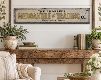 Op de afbeelding: Een rechthoekig horizontaal wandbord met een verweerde gebroken witte achtergrond en een zwarte rand. De tekst luidt THE ANDREW'S MERCANTILE & TRADING CO. in dikke zwarte en gele letters, met de zin Family Owned & Operated eronder.