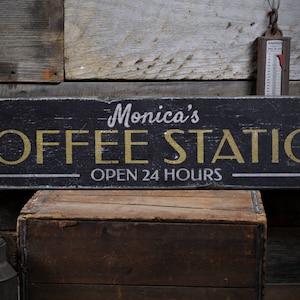 Może przedstawiać: Czarny drewniany znak z białymi i złotymi literami, na kt&oacute;rym widnieje napis "Monica's Coffee Station Open 24 Hours".