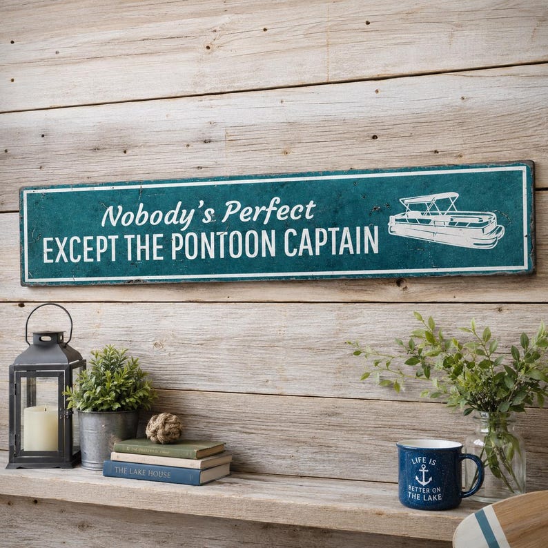 Op de afbeelding: Een rechthoekig blauwgroen bord met een witte rand en witte tekst die Nobody's Perfect EXCEPT THE PONTOON CAPTAIN luidt, voorzien van een witte lijntekening van een pontonboot aan de rechterkant tegen een verweerde achtergrond.