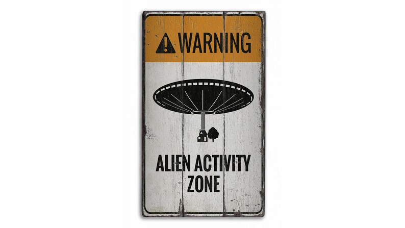 May include: A white wooden sign with black text and a black silhouette of a UFO. The sign reads "WARNING ALIEN ACTIVITY ZONE".