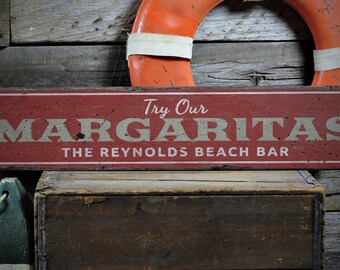 May include: Red wooden sign with white lettering that reads "Try Our Margaritas The Reynolds Beach Bar".