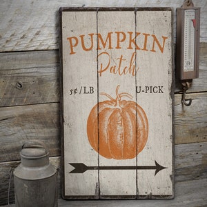 May include: A rustic wooden sign with white paint and black lettering that reads "Pumpkin Patch" with a price of $ per pound and a black arrow pointing to the right. The sign also features a vintage illustration of an orange pumpkin.