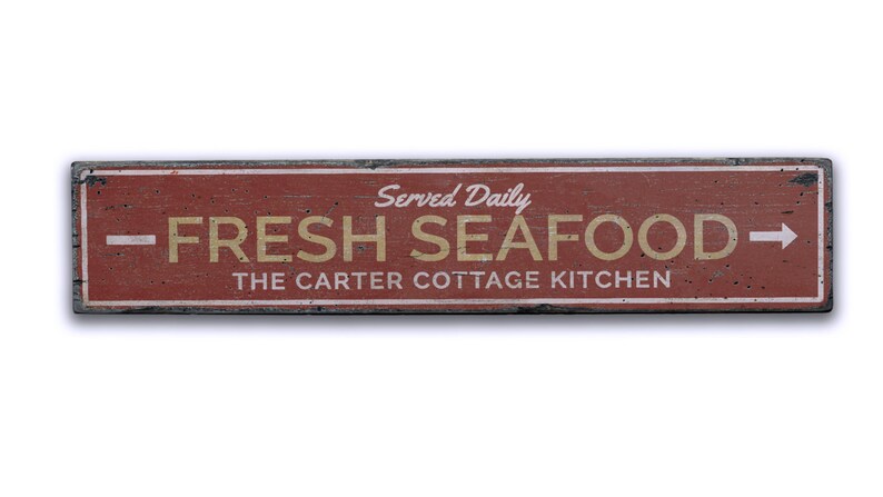 May include: A red wooden sign with white and black trim, advertising "Fresh Seafood" served daily at "The Carter Cottage Kitchen".