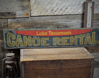 Könnte beinhalten: Ein vintage Holzschild mit blauer, grüner, gelber und roter Farbe. Das Schild trägt die Aufschrift "Lake Tecumseh Canoe Rental".