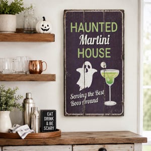May include: A rectangular wooden wall sign with a dark purple background featuring the text HAUNTED Martini HOUSE and Serving the Best Boos Around in white and green. A white ghost and a green martini glass with a skull garnish are illustrated.