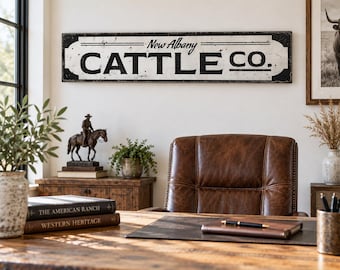 May include: A rectangular wall sign with a distressed white background and black border featuring the text New Albany CATTLE CO. in a bold serif font. The sign has a weathered finish with visible dark edges and horizontal lines above the text.