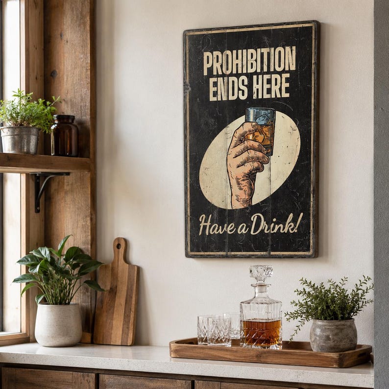 May include: A rectangular wall sign with a black background and distressed edges. It features the text PROHIBITION ENDS HERE in white, a central illustration of a hand holding a glass of amber liquid, and the text Have a Drink! in white.