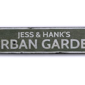 May include: A weathered green wooden sign with white lettering that reads "Jess & Hank's Urban Garden".
