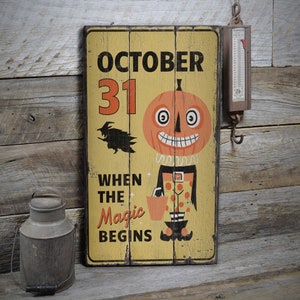 May include: A yellow wooden sign with black lettering that reads "October 31 When the Magic Begins". A cartoon pumpkin with a toothy grin and a witch's hat is in the center of the sign.