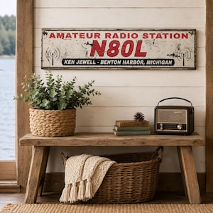 May include: A rectangular metal sign with a distressed white finish, featuring the red text AMATEUR RADIO STATION, the call sign N80L in large red letters, and the black text KEN JEWELL - BENTON HARBOR, MICHIGAN, along with black radio tower icons.
