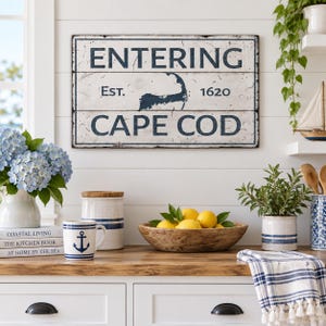 May include: A rectangular white wall sign with dark blue text reading ENTERING CAPE COD and EST. 1620, featuring a dark blue silhouette of the Cape Cod peninsula. The sign has a distressed finish with visible horizontal lines and a dark blue border.