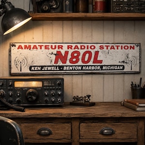 May include: A rectangular metal sign with a distressed white finish, featuring the red text AMATEUR RADIO STATION N80L and the black text KEN JEWELL - BENTON HARBOR, MICHIGAN. The sign includes black radio tower icons on both the left and right sides.
