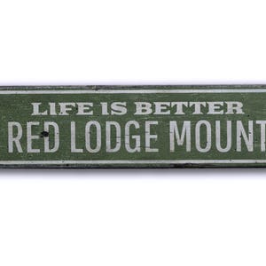 May include: A green wooden sign with white text that reads "Life is better on Red Lodge Mountain".