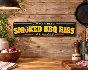 May include: A rectangular black metal sign with yellow and red lettering that reads "JIMMY'S BEST SMOKED BBQ RIBS He's Smokin'!" The sign features a distressed finish with visible wear along the edges and surface, presenting a vintage aesthetic.