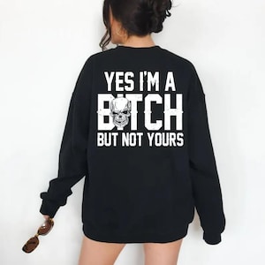 May include: Black sweatshirt with the text "YES I'M A BITCH BUT NOT YOURS" in white block letters. A white skull graphic is centered within the word "BITCH". The sweatshirt is worn by a person with dark hair.