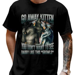 May include: Black t-shirt featuring a graphic of three anthropomorphic wolves with the text "GO AWAY KITTEN, YOU DON'T WANT TO SEE DADDY LIKE THIS *GROOWLS*". The wolves are in various poses, with one wearing a cowboy hat.