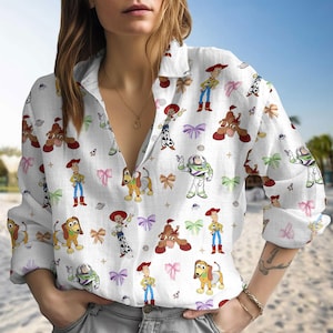 May include: A white long-sleeved button-down shirt with a v-neck. The shirt features a repeating pattern of characters from the Toy Story film franchise, including Woody, Buzz Lightyear, Jessie, and Slinky Dog.