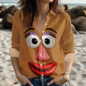 May include: A button-down shirt with a cartoon face design. The shirt features large eyes with purple eyeshadow, a pink nose, and red lips. The shirt is brown with a textured appearance and has beige cuffs.