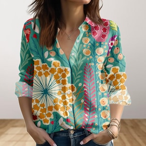May include: A button-down shirt with a vibrant floral pattern in shades of teal, yellow, pink, and white. The long-sleeved shirt features a V-neck and is paired with blue jeans. The cuffs are rolled up, revealing a patterned interior.