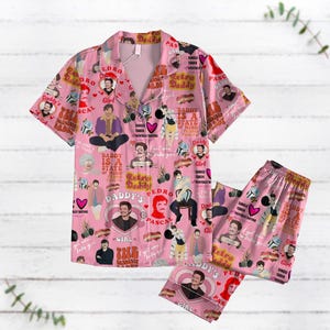 Puede incluir: Conjunto de pijama rosa con una camisa de manga corta y pantalones largos. La tela presenta un patrón repetido de la cara de un hombre con el texto "Daddy's Pedro Pascal" y "Retro Daddy".