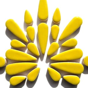 May include: A collection of bright yellow, teardrop-shaped objects arranged in a radial pattern against a white background. The objects vary in size, with some elongated and others more compact. The arrangement creates a visually striking design.