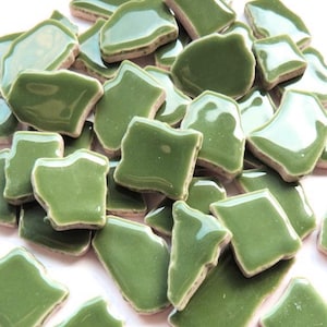 May include: A collection of irregularly shaped, glossy green ceramic tiles. The tiles have a smooth, reflective surface and a slightly rough, unglazed edge. The pieces vary in size and shape, suitable for mosaic projects.