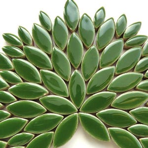 May include: A collection of glossy, leaf-shaped ceramic tiles in a vibrant green hue. The tiles are arranged in a fan-like pattern, creating a decorative mosaic design. The tiles are approximately 2 inches long.