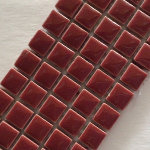 May include: A collection of small, square, burgundy-colored tiles arranged in a diagonal pattern. Each tile has a glossy finish and is set against a white background. These tiles are suitable for various home decor projects.