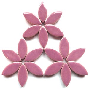 May include: A set of 12 pink ceramic flower-shaped tiles. The tiles are arranged in a symmetrical pattern, forming a flower shape.