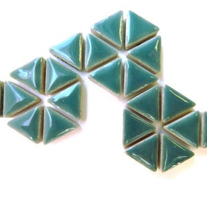 May include: A collection of teal-colored, triangular ceramic tiles arranged on a white surface. Each tile has a glossy finish and a slightly rounded shape. The tiles are grouped in clusters, showcasing their geometric form.